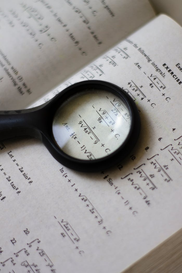 A magnifying glass focuses on mathematical equations in a textbook, highlighting detailed calculations.
